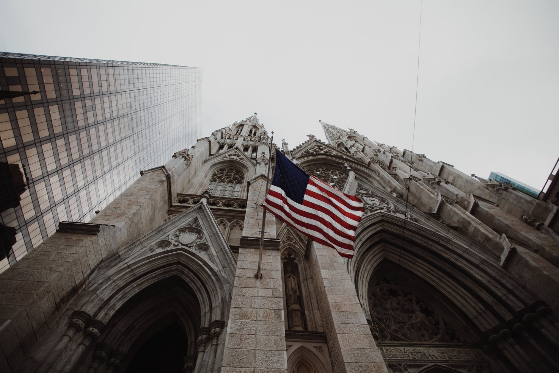 low angle photography of waving usa flag on brown concrete cathedral